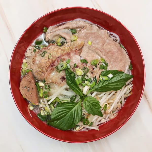 A red bowl of Krungthep Thai and Pho's pho with beef, noodles, sprouts, and basil.