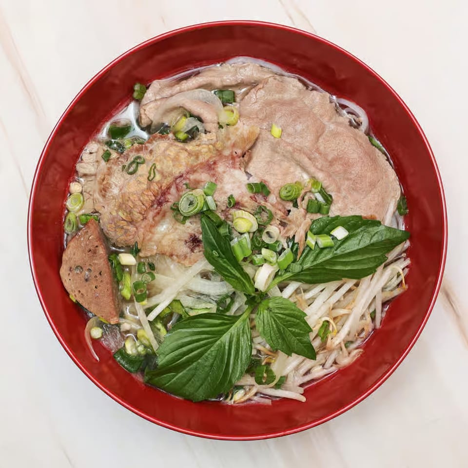 A red bowl of Krungthep Thai and Pho's pho with beef, noodles, sprouts, and basil.