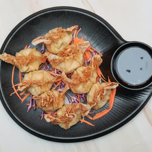 Golden fried wontons with shredded carrots and purple cabbage, served with a dark dipping sauce.