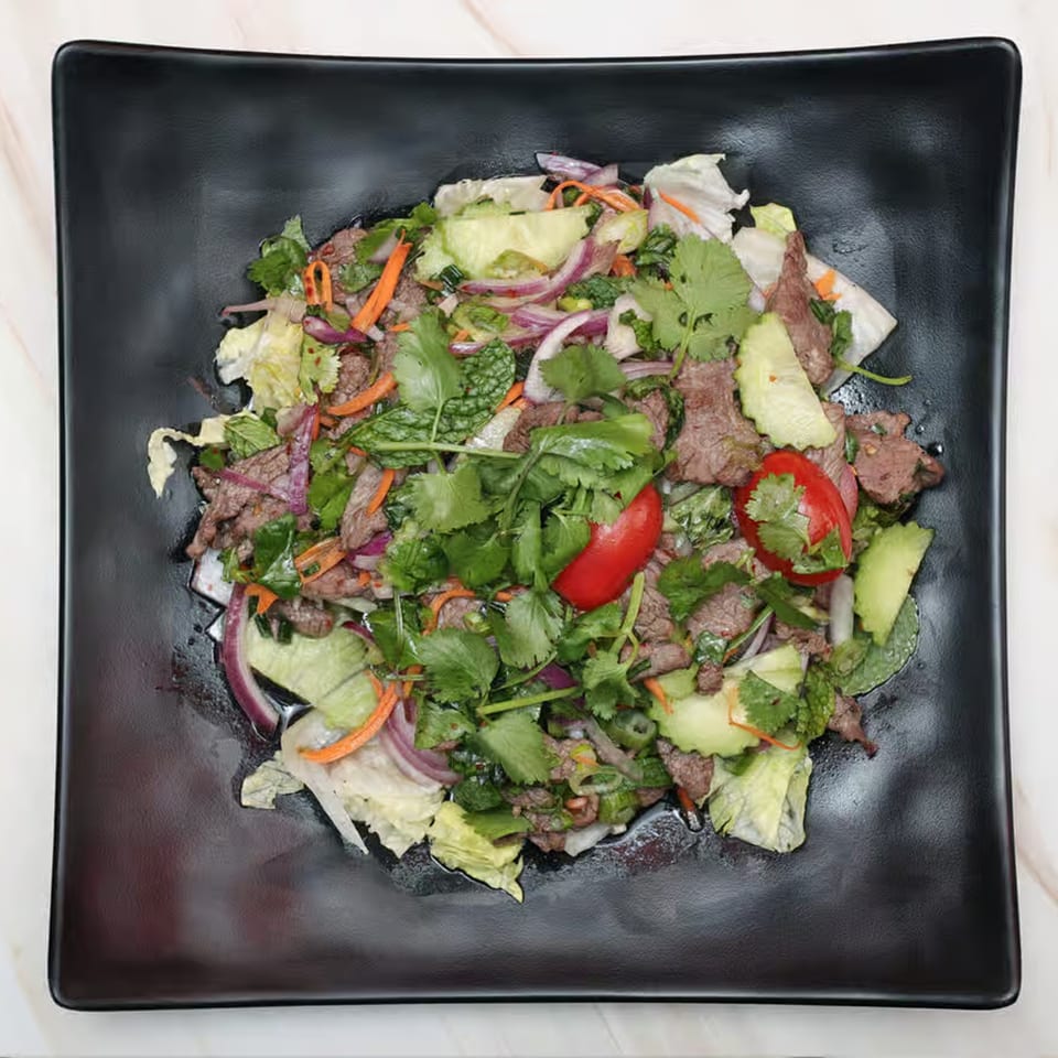 Top-down view of a Thai beef salad with red onions, cilantro, mint, and red chilies.